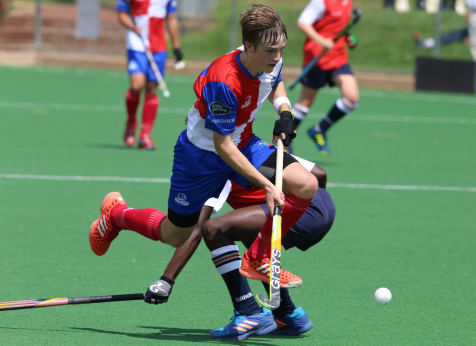 Field hockey player in mid-action during a competitive match, skillfully maneuvering the ball while evading an opponent, showcasing athleticism and agility on a turf field.